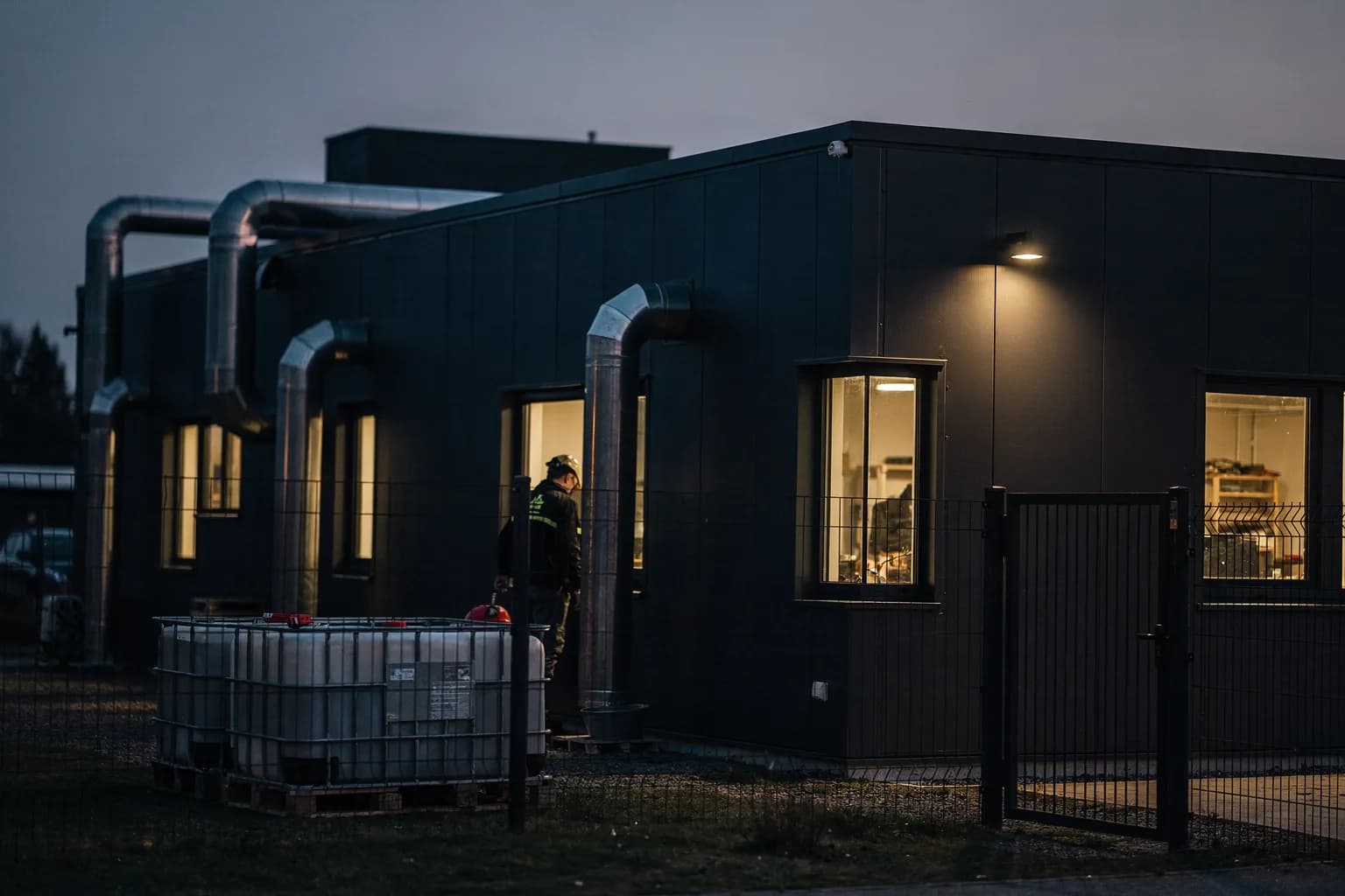 Kompaktes Industriegebäude in der Dämmerung mit Abluftkanälen und beleuchteten Fenstern, kleiner Hof