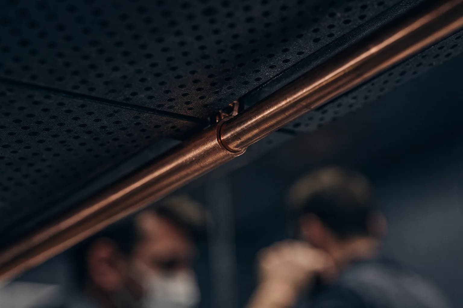 Extreme Nahaufnahme eines Kupferkapillarrohrs, das in die Sicke eines perforierten Metalldeckenpaneels gedrückt ist, sehr geringe Schärfentiefe