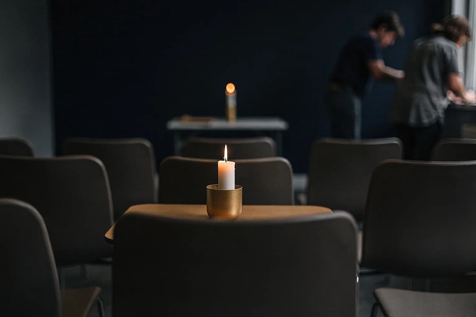 Stiller Abschiedsraum mit Reihen schlichter Stühle und einem kleinen Tisch mit einer einzelnen Kerze, Tageslicht, leer