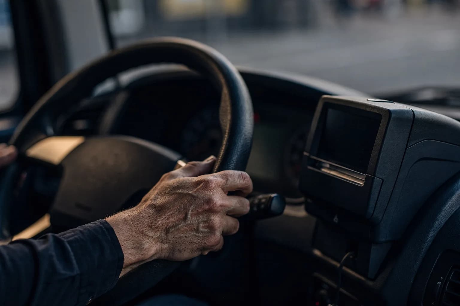 Nahaufnahme eines Busfahrerplatzes mit Lenkradkranz und einem Ticketdrucker, eine Hand am Lenkrad, keine lesbare Anzeige, geringe Schärfentiefe