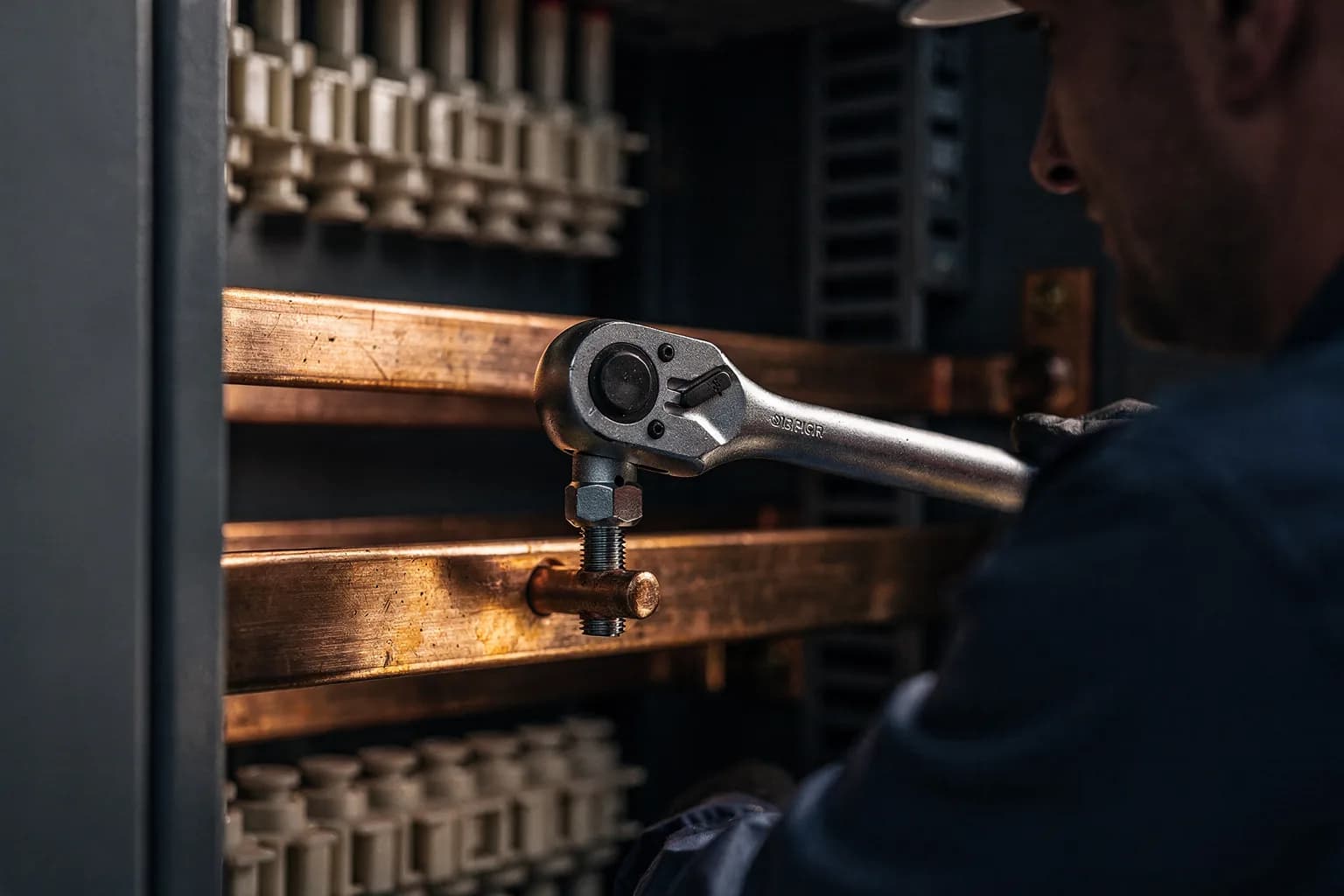 Drehmomentschlüssel an einer Sammelschienenverschraubung in einem geöffneten Schaltschrank, Kupfer und Isolatoren, kühles Licht