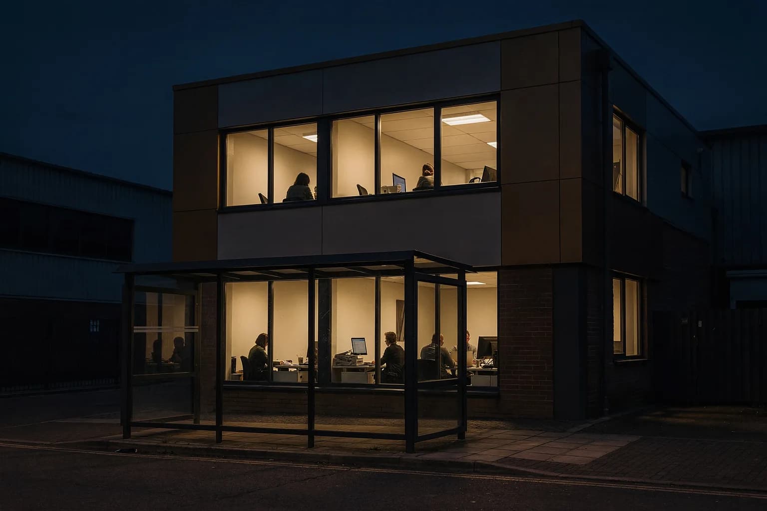 Kleines Bürogebäude in der Dämmerung mit beleuchteten Fenstern im ersten Stock, Gewerbegebietsstraße, eine Bushaltestelle davor