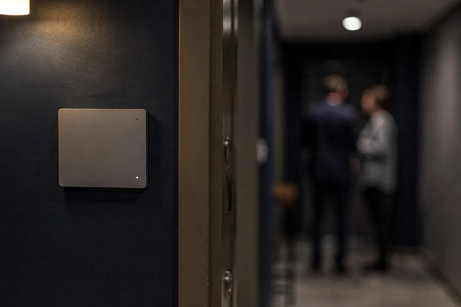 Rufanlagen-Bedienfeld an der Wand neben einer Wohnungstür im Flur einer Residenz, dezent und unbeschriftet, warmes Wandlicht