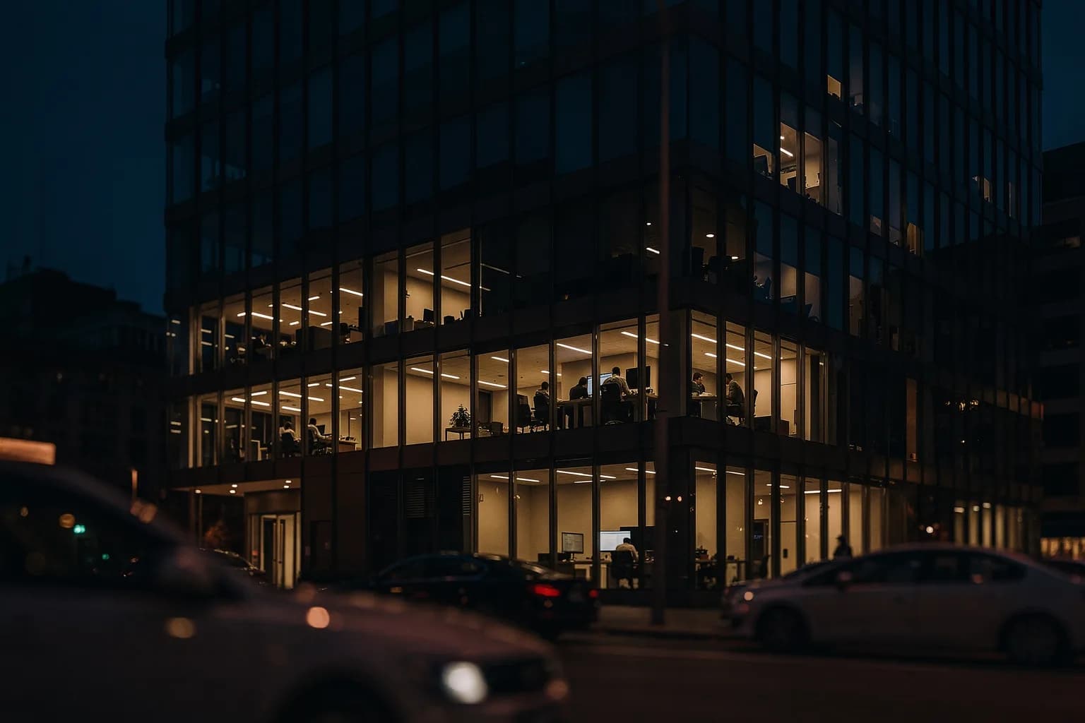 Bürogebäude in der Dämmerung mit einer beleuchteten Etage, ruhige Straße mit parkenden Autos