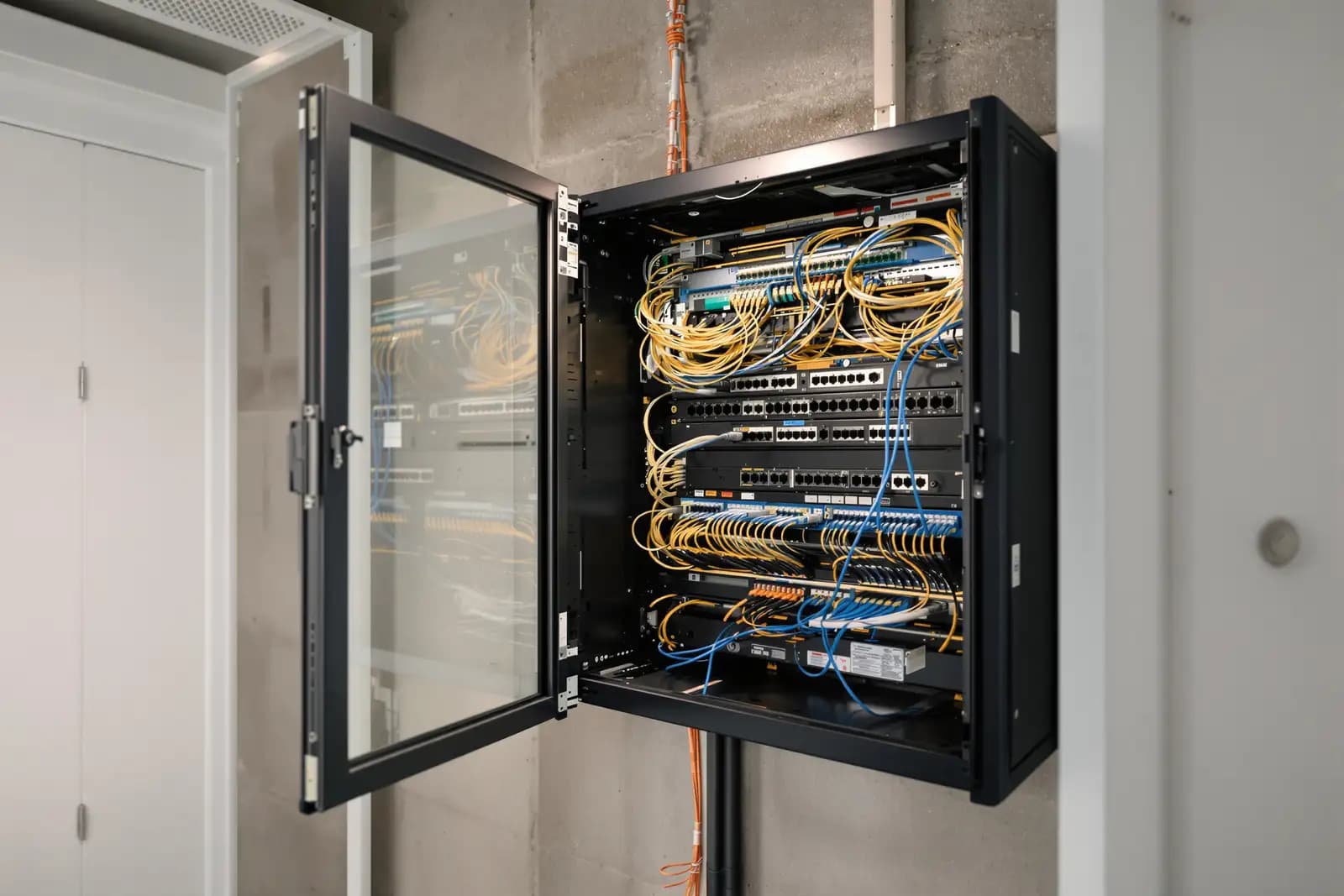 Netzwerkschrank an der Wand eines unfertigen Technikraums, Rangierfelder und Kabelpritschen, Sichtbeton
