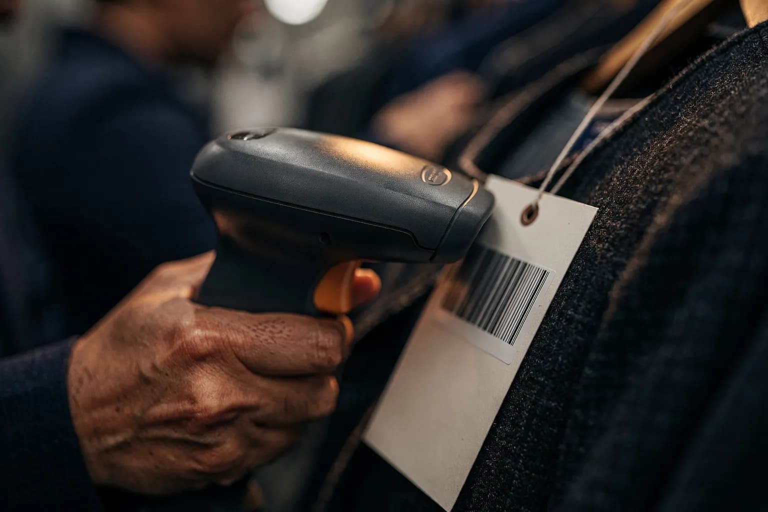 Handscanner an einem Anhängeetikett eines Kleidungsstücks, die Gewebestruktur im Fokus