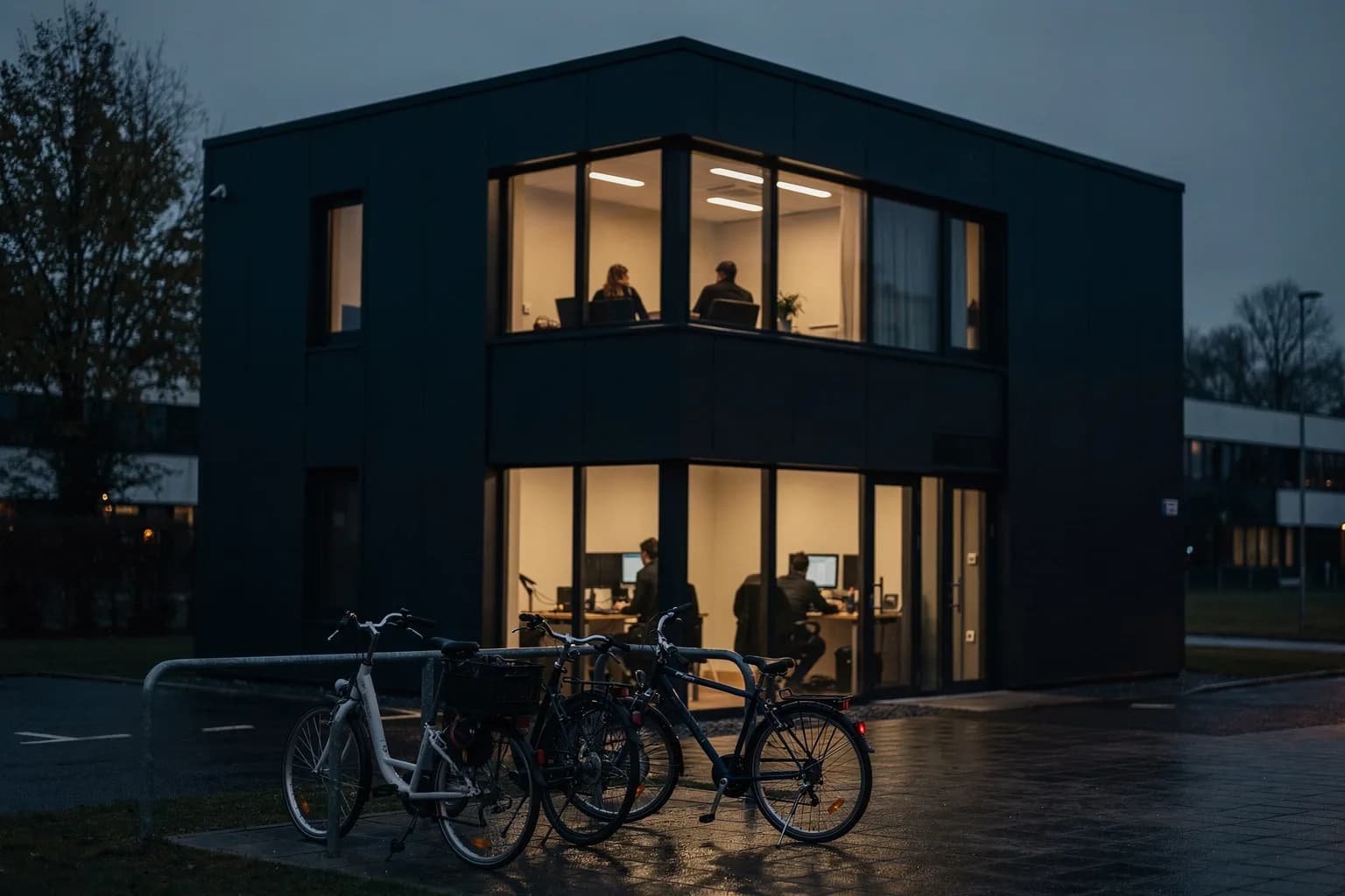 Kleines Technikgebäude in der Dämmerung in einem Gewerbepark, eine beleuchtete Etage, abgestellte Fahrräder