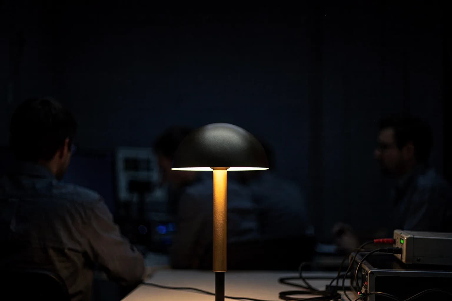 Dunkler lichttechnischer Prüfraum mit einer einzelnen brennenden Leuchte auf einem Stativ, das Licht verliert sich in der Schwärze