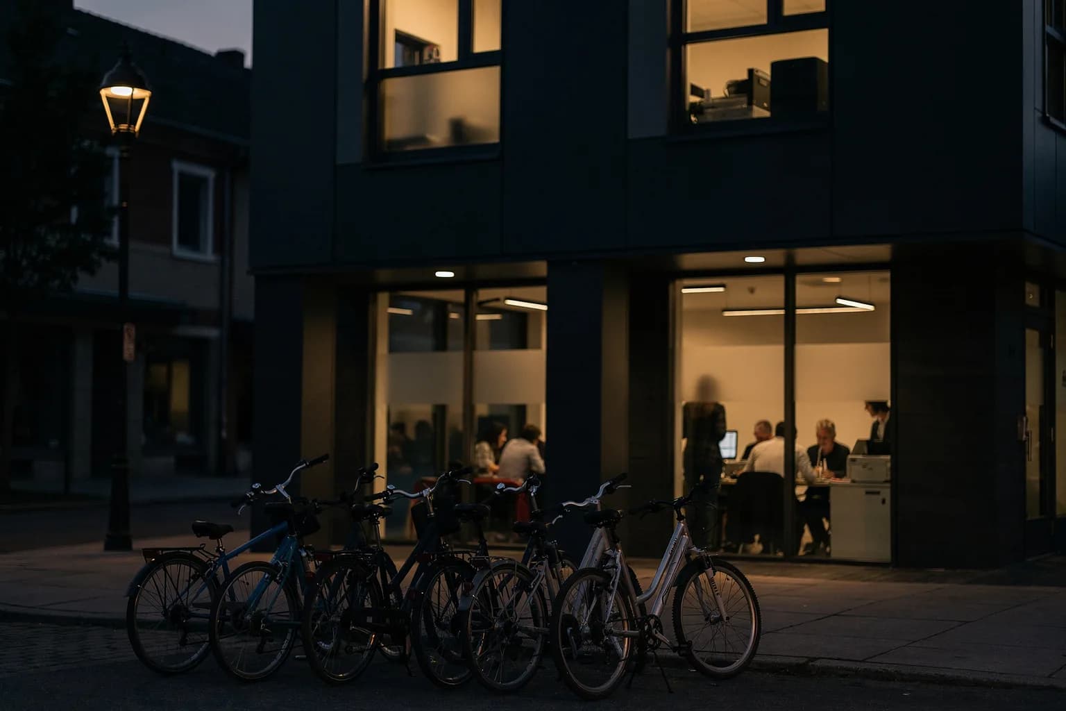 Bürogebäude in der Dämmerung an einer Straße in einer Kleinstadt, zwei Etagen beleuchtet, abgestellte Fahrräder am Eingang