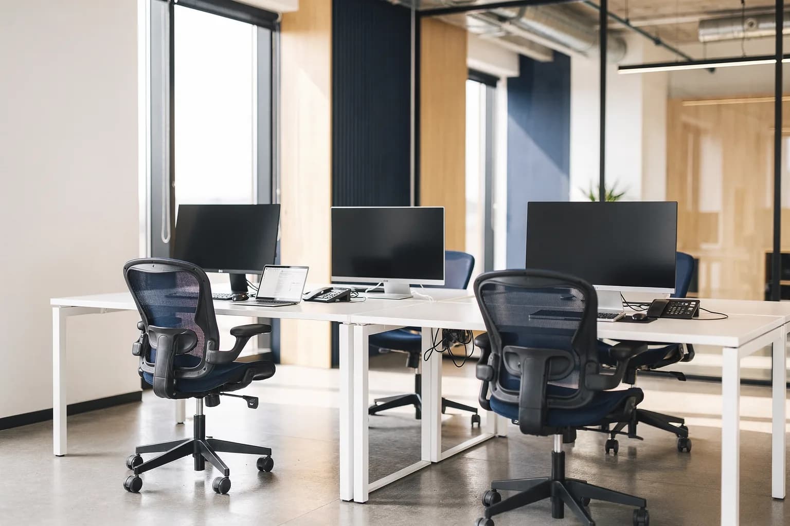 Helles Büro mit mehreren aufgeräumten Schreibtischen, Bildschirmen und Tischtelefonen