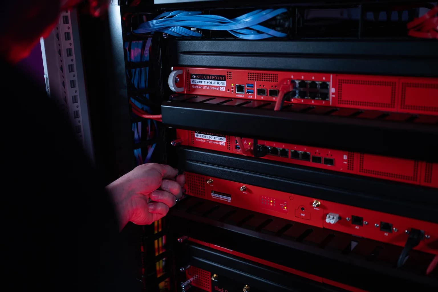 Mehrere Securepoint NextGen UTM-Firewalls der RC-Serie übereinander im 19-Zoll-Serverschrank eingebaut, rote Gehäuse, ein Gerät wird gerade eingesetzt