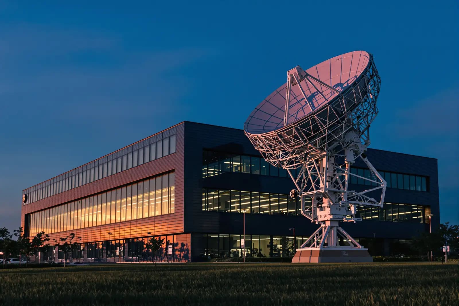 Bürogebäude eines Technologieparks mit großer Satellitenantenne dahinter im Abendlicht