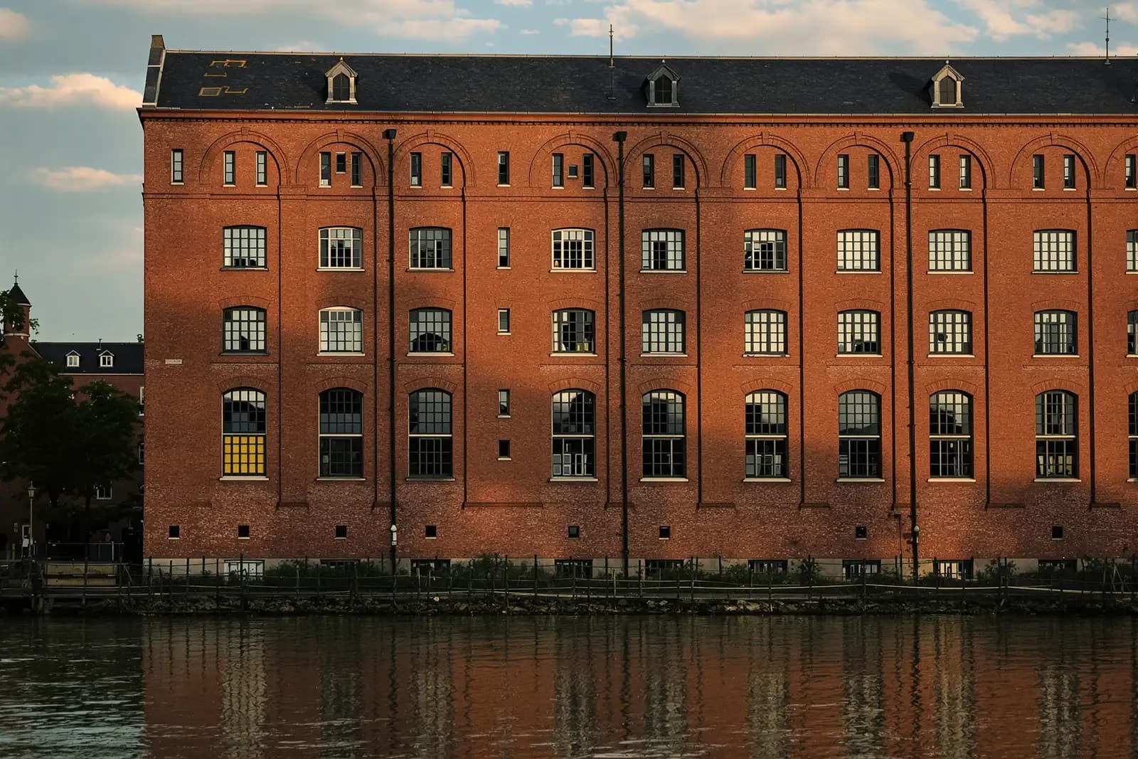 Altes Backsteinfabrikgebäude am Flussufer mit hohen Fenstern im späten Nachmittagslicht